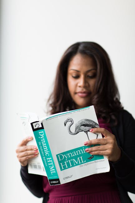 A woman with dark hair, dressed in a black blazer and a dark purple top, is holding a book titled 'Dynamic HTML' published by O'Reilly. The book features a cover with a photographic image of a flaming